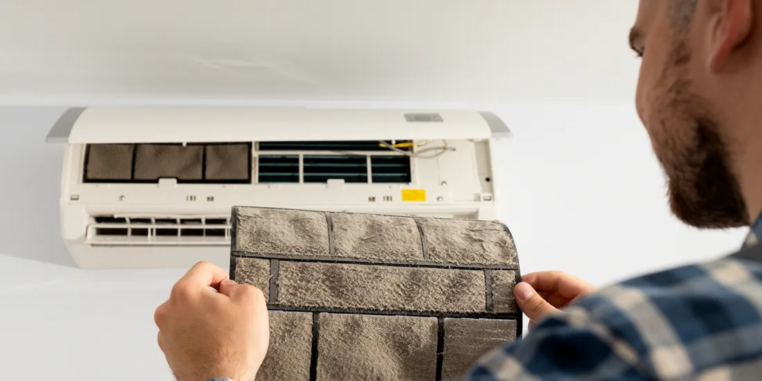 Homeowner removing a clogged, dust-caked air filter from a wall-mounted AC unit
